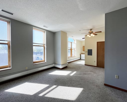 an empty living room with a ceiling fan and windows