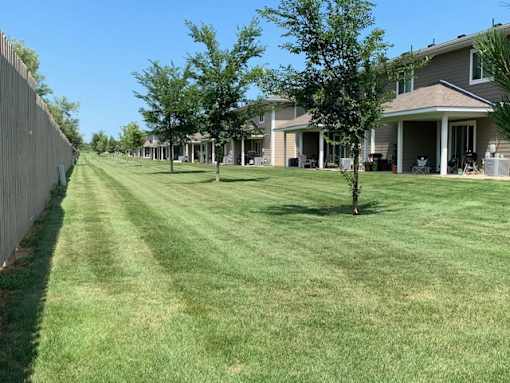 A residential street with houses on both sides and a person walking on the grass.