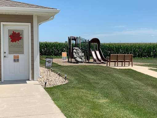 A playground with a slide, a bench and a sign in front of a house.