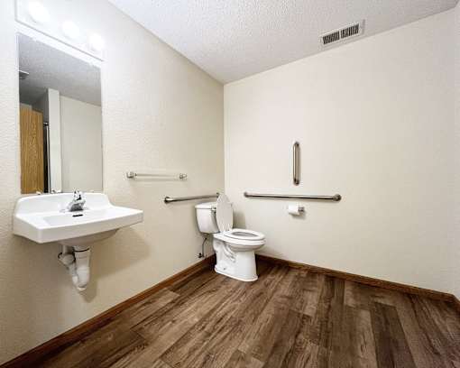 A white toilet sits in a small bathroom with wood flooring.