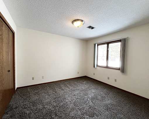 A room with a carpeted floor and a window with blinds.