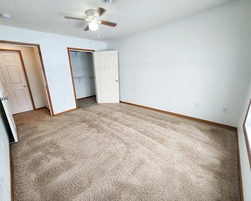 A room with a carpeted floor and a ceiling fan.