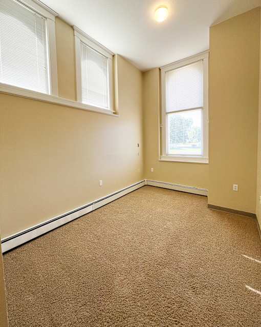 A room with a carpeted floor and two windows.