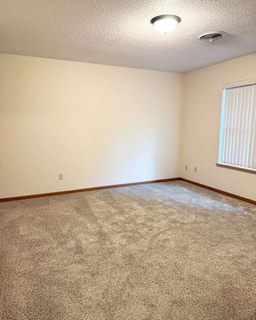 A room with a carpeted floor and a window with blinds.