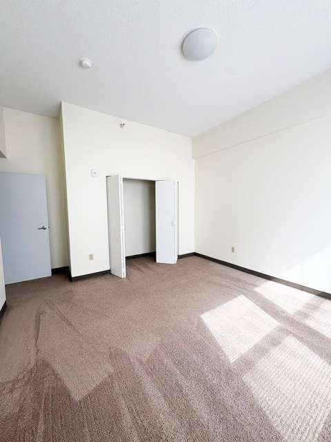 A room with a carpeted floor and a white ceiling with a smoke detector.