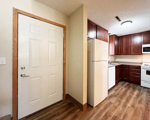 A white door is open to a kitchen with brown cabinets.