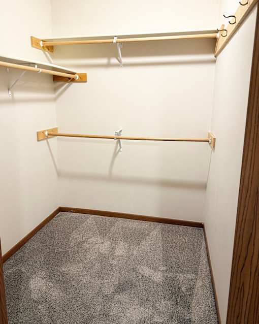 A walk in closet with a grey carpet and two shelves.