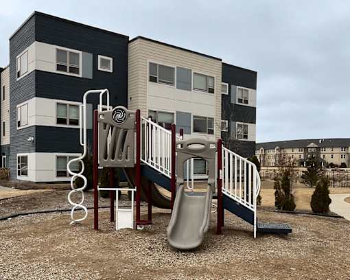 A playground with a slide and a climbing frame in front of a modern building.