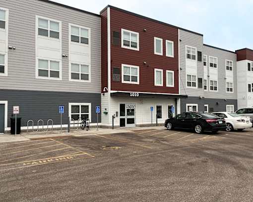 A parking lot in front of a multi-story apartment building with a black car parked in the lot.