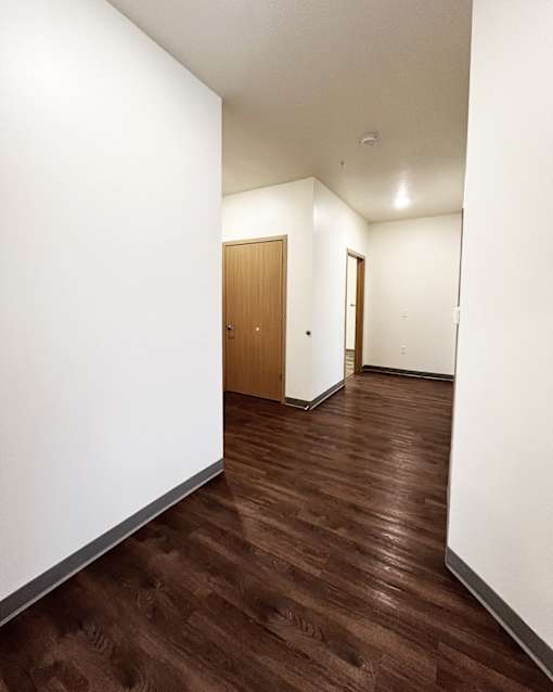 A hallway with a brown wooden floor and white walls.