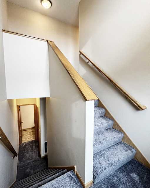 A staircase with a grey carpeted runner and wooden handrails.