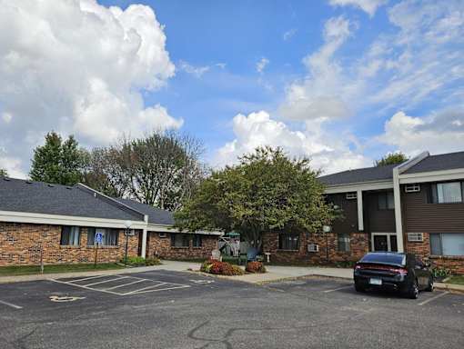 A black car is parked in a parking lot in front of a brick building.