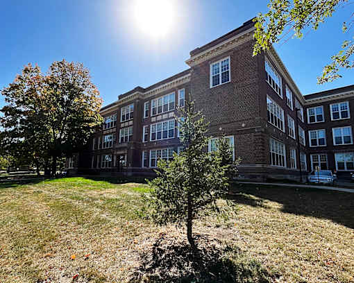 A sunny day at a brick building with trees in front.