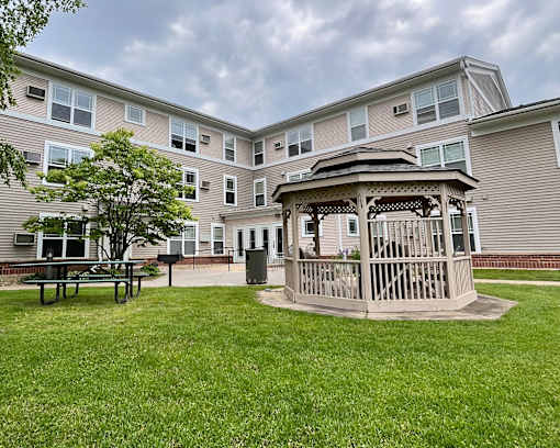 A gazebo sits in the middle of a grassy area in front of a building.