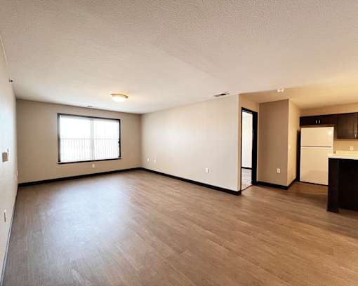 A spacious room with wooden flooring and a kitchen area to the right.