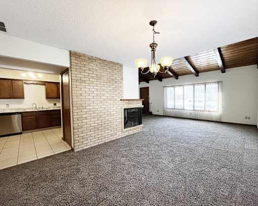A living room with a fireplace and a kitchen area in the background.
