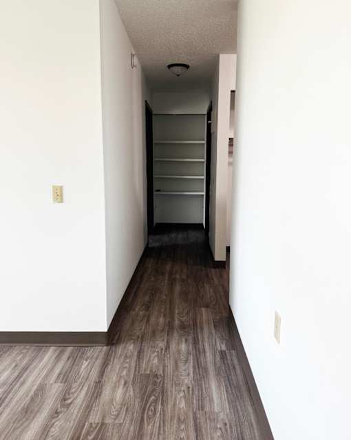 A long hallway with a wood floor and a white wall.