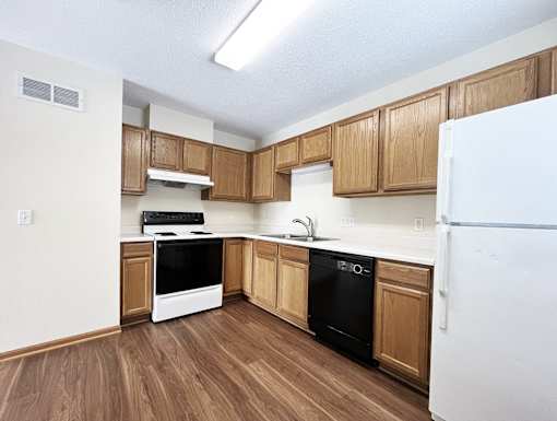 an empty kitchen with wood flooring and white appliances