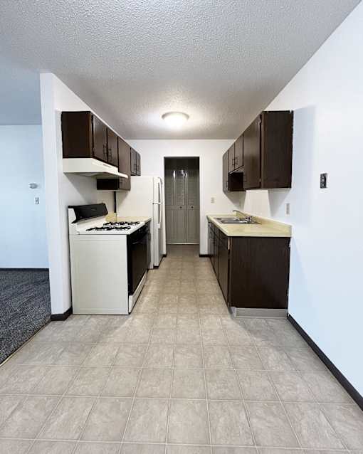an empty kitchen with white appliances and brown cabinets