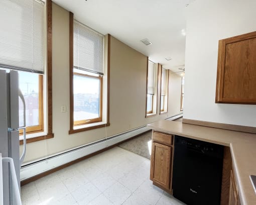 an empty kitchen with windows and a counter top and a refrigerator