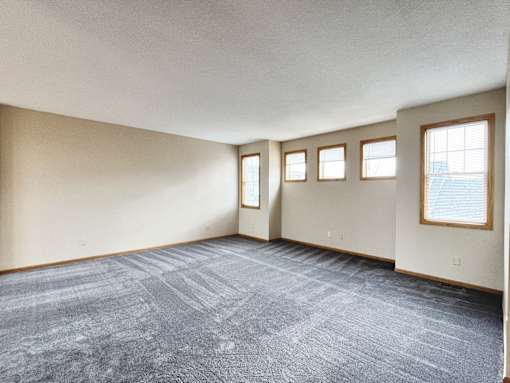 A room with a carpeted floor and three windows.