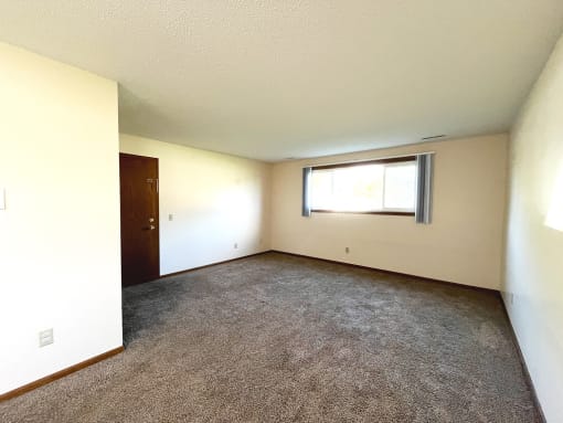 an empty living room with a window and carpet