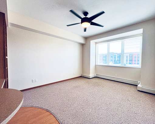 A room with a ceiling fan and a window overlooking a city.