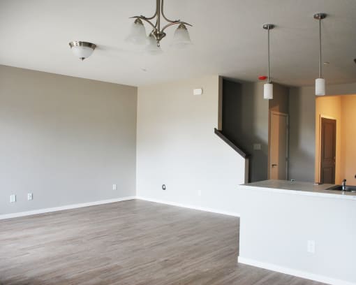 an empty living room with a kitchen in the background