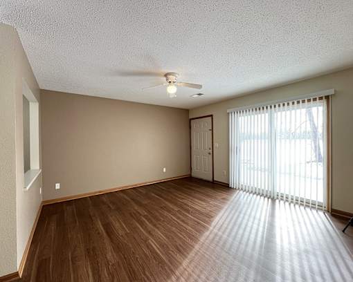 an empty living room with a large window and a ceiling fan