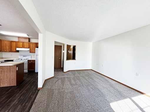 an empty living room and kitchen with wood flooring and white walls
