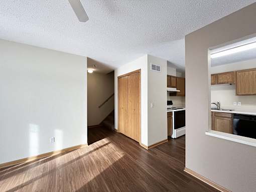 an empty living room with wood flooring and a kitchen