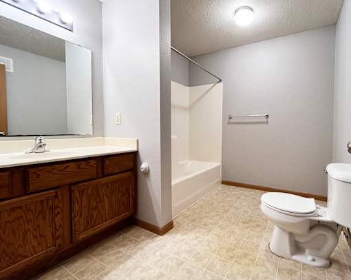 A white toilet sits in a bathroom with a white sink and a walk-in shower.