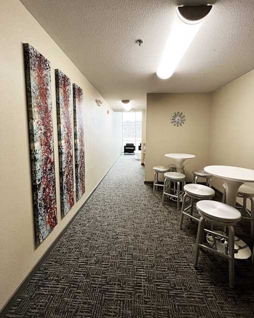 A hallway with a carpeted floor and a row of stools and tables on the right.