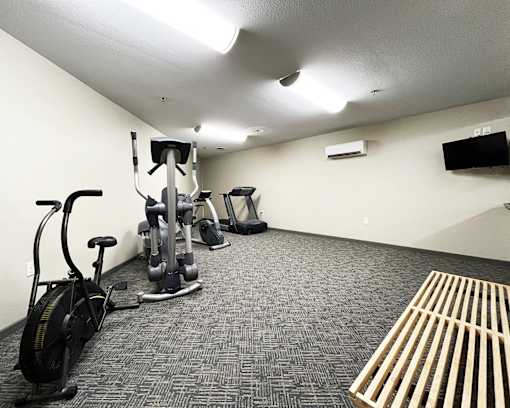 A gym with a variety of equipment including a stationary bike, a treadmill, a weight bench, and a flat screen TV mounted on the wall.