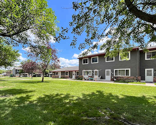 A tree in front of a building with a lawn in front of it.