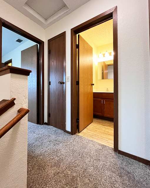 A hallway with a carpeted floor and a staircase on the left side.