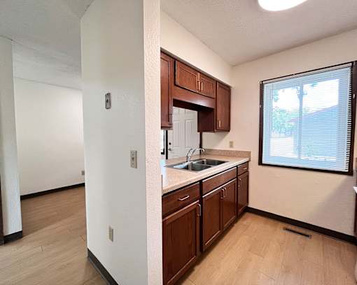 A kitchen with wooden cabinets and a window with blinds.