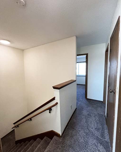 A staircase with a wooden handrail and a carpeted floor.