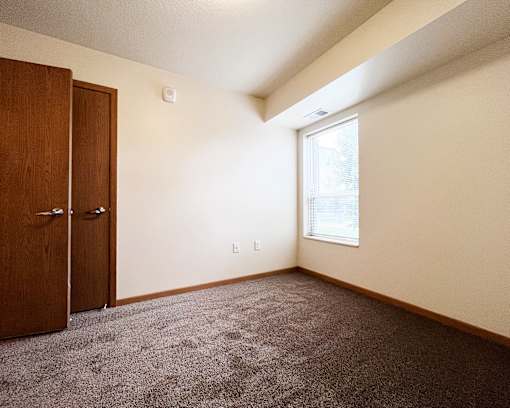 A room with a carpeted floor, a window, and a wooden door.