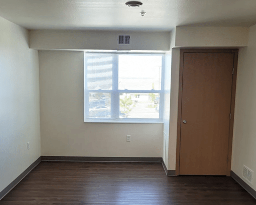 A room with a brown door and a window with blinds.