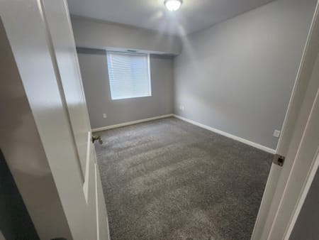 A room with a carpeted floor and a window with blinds.