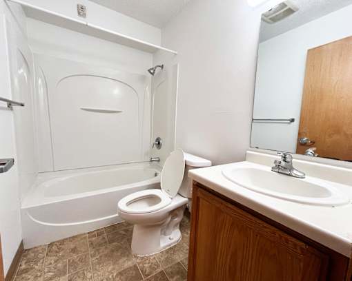 A white toilet is in a bathroom with a white tub and sink.
