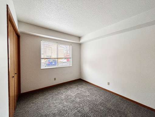 A room with a carpeted floor and a window with blinds.
