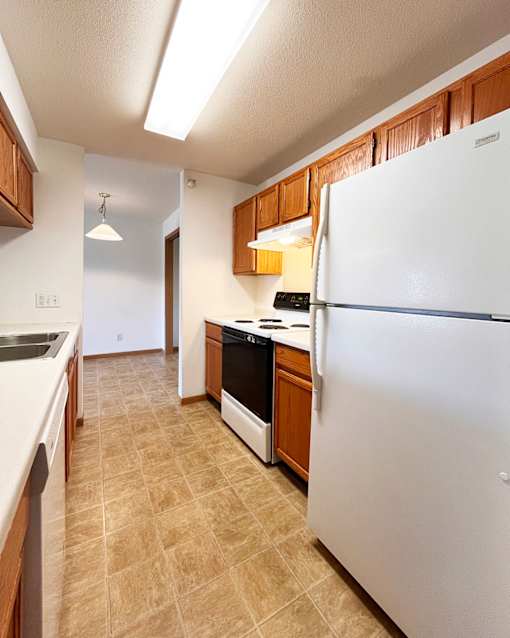 A kitchen with a white refrigerator, brown cabinets, and a tiled floor.