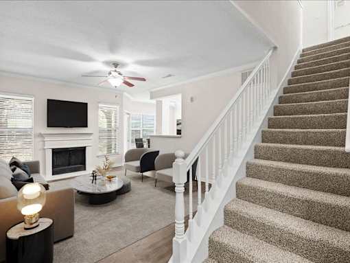A living room with a fireplace, a ceiling fan, and a staircase. at Crescent Apartment Homes, Kansas, 66219