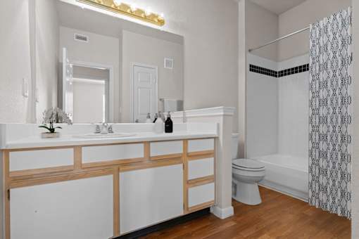 A bathroom with a tub shower combo, a large vanity mirror, plenty of counter space, and storage cabinets and drawers under the sink. at Crescent Apartment Homes, Lenexa, 66219
