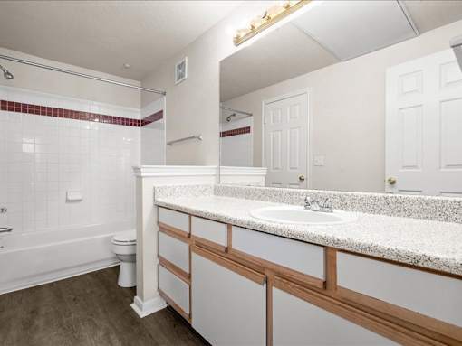 A large bathroom with a shower and bath tub combo and a large vanity mirror with lots of counter space and storage under the sink. at Crescent Apartment Homes, Lenexa, KS