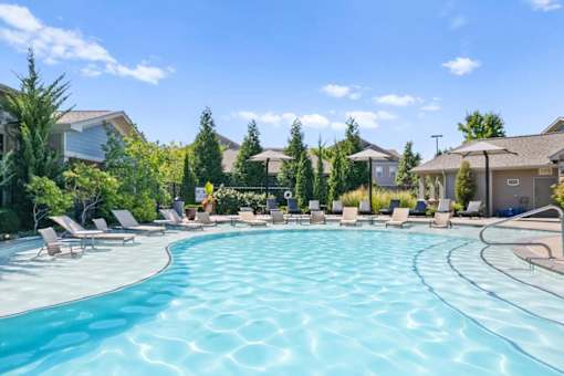 a swimming pool with chaise lounge chairs and umbrellas in front of a row of at Stonepost Crossing Apartments, Overland Park, Kansas