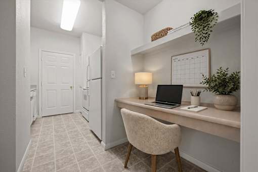 Close-up of built-in desk area with laptop workspace, overhead shelving, and decorative accents near the kitchen in a Crescent Apartments unit.