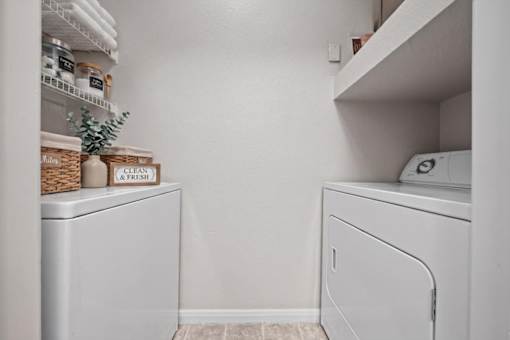 In-unit full-size washer and dryer set with overhead shelving and storage space inside a laundry closet at Crescent Apartments in Lenexa, KS.